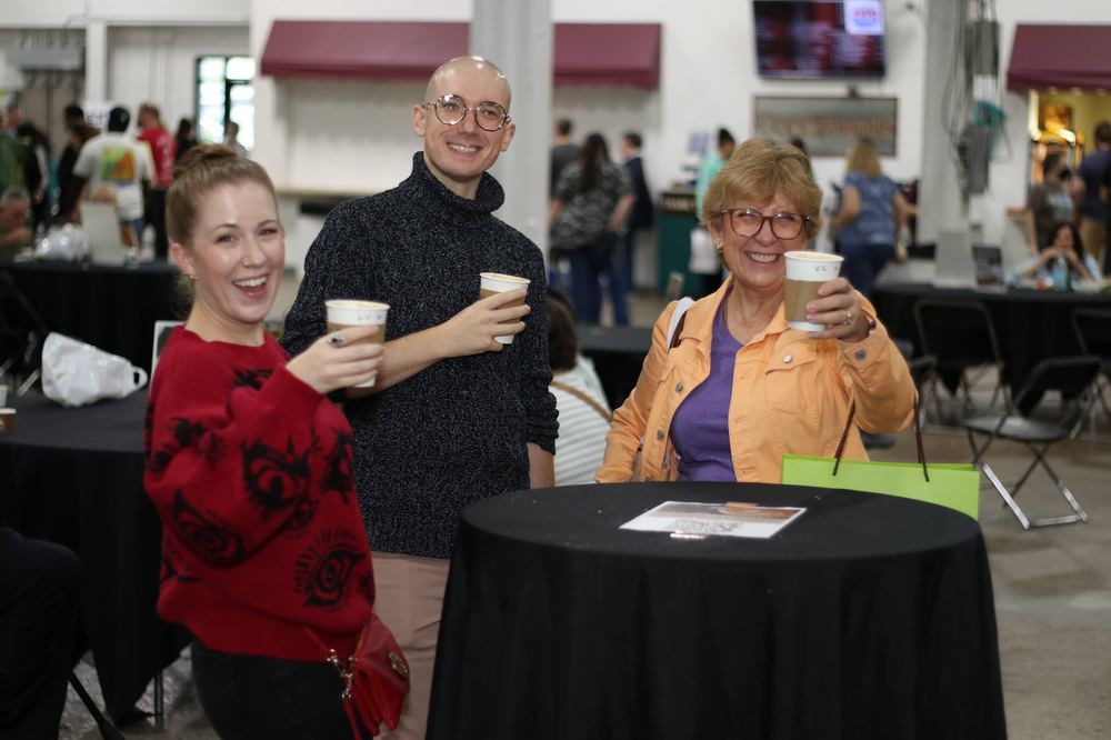 Three friends laughing together with drinks in hand at the festival.